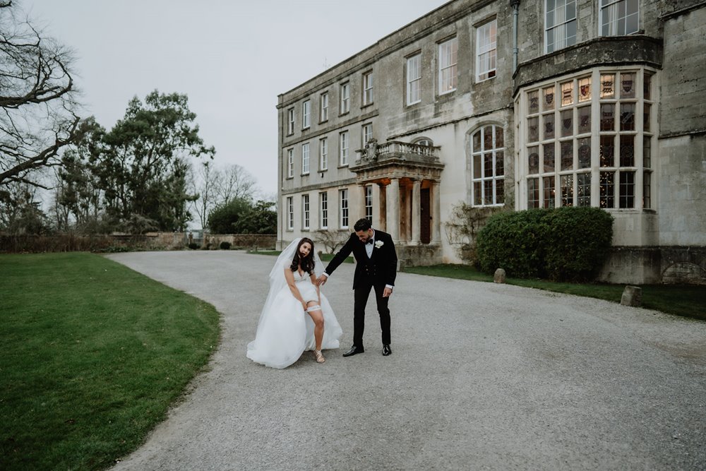 Gangster bride and groom posing outside stately home wedding venue bride lifting dress to show garter