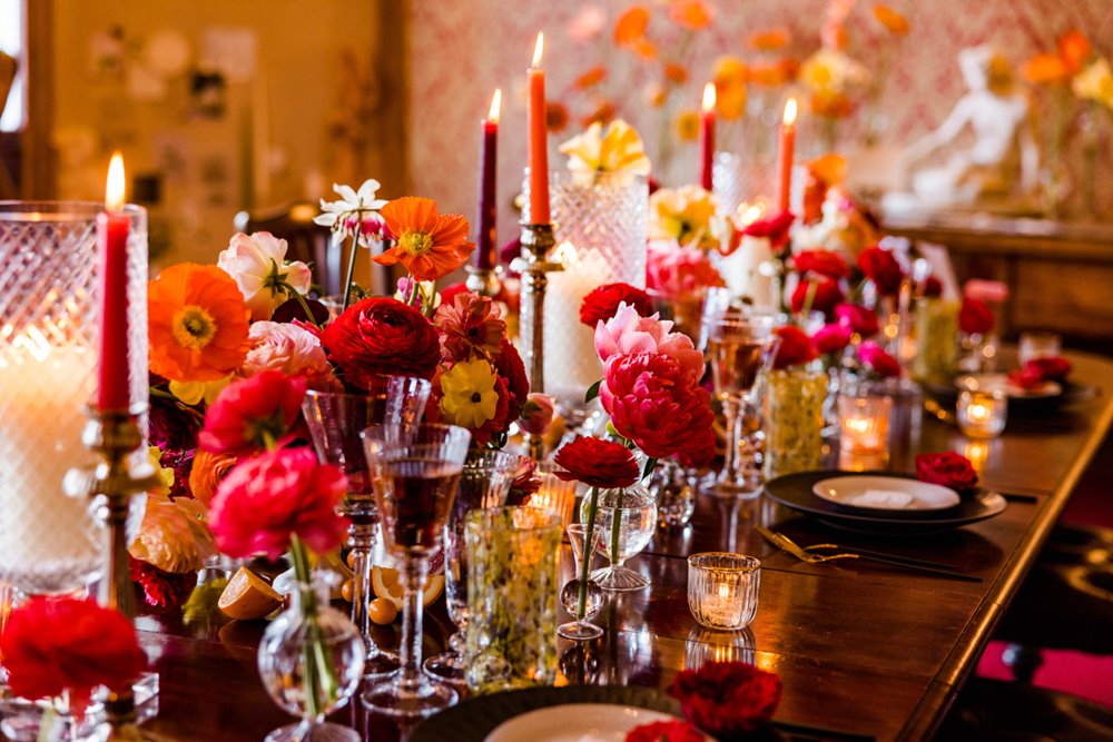 Pink and red wedding inspiration with bold flowers and candles with mismatching glass wear on table in dining room at unusual wedding venue elmore court