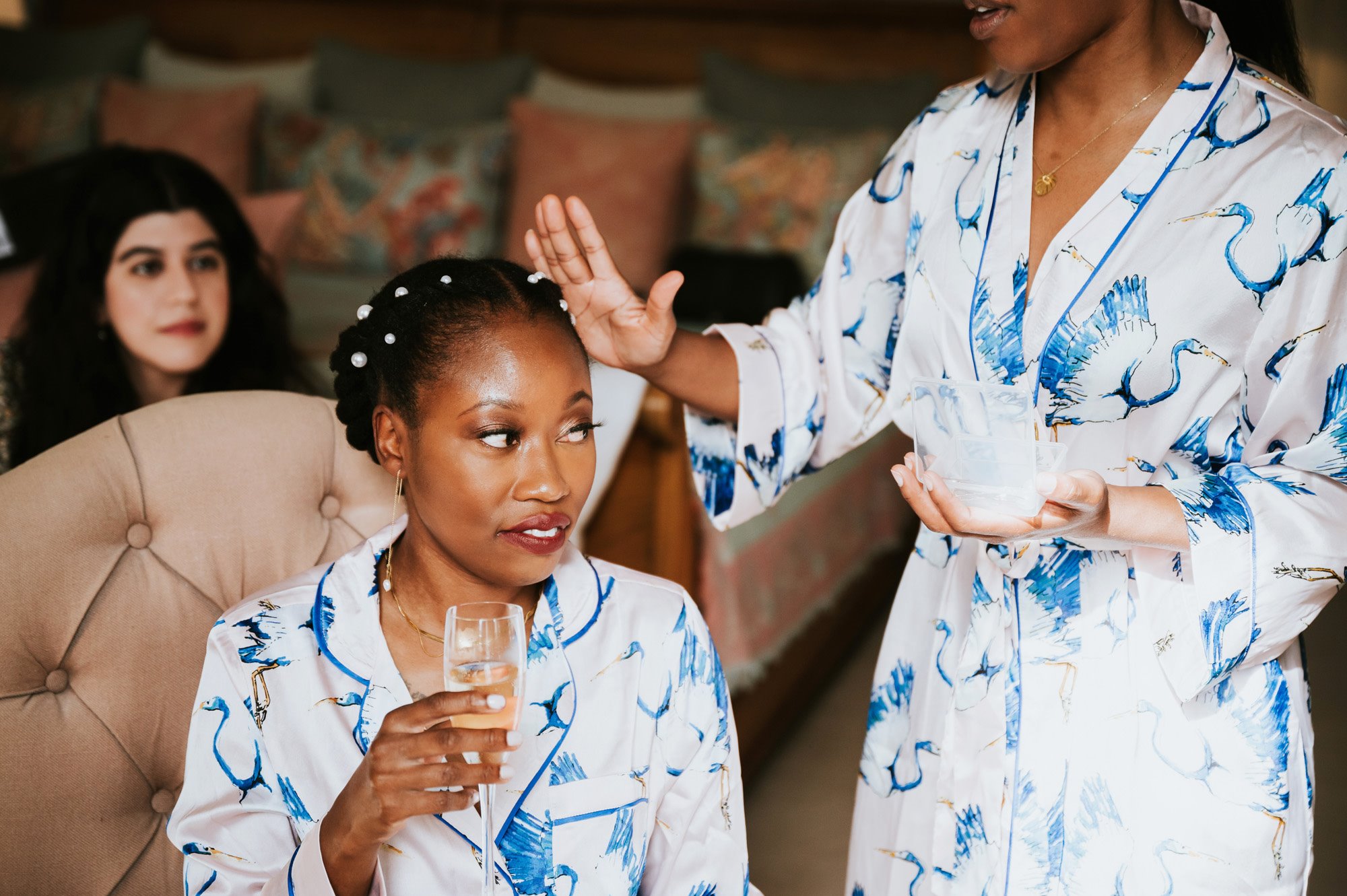 Beautiful black bride having her hair pinned with pearls by sister in matching silk pyjamas on wedding morning at stately home elmore court