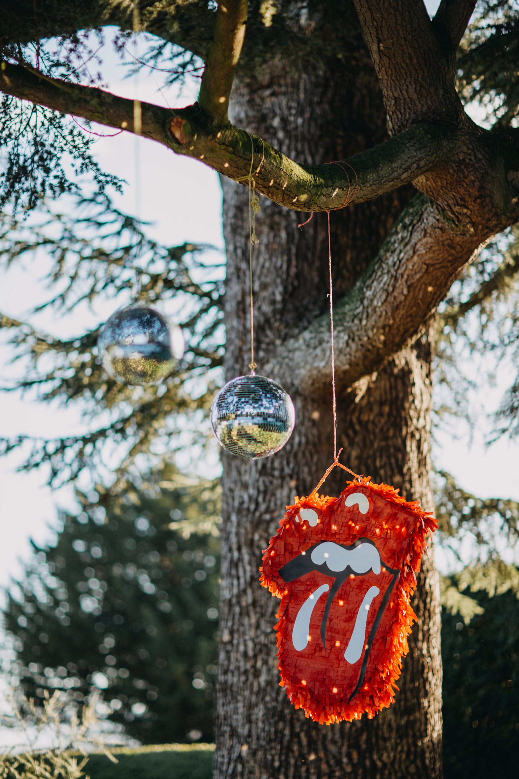 Cool rock n roll style wedding with rolling stones pinata and disco ball hanging from tree in the cotswolds