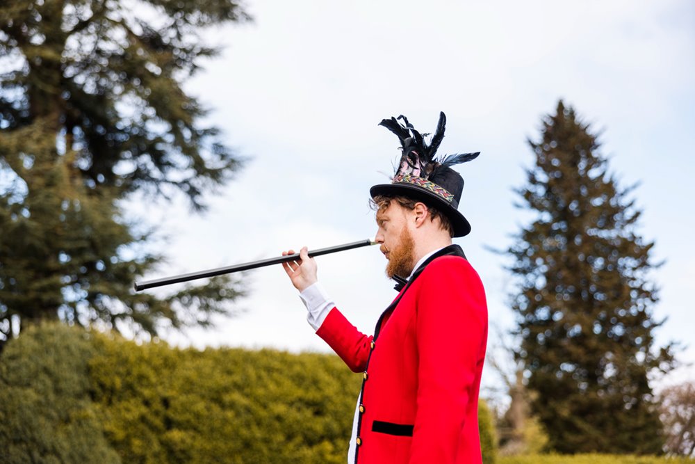 Circus performer in top hat and red coat entertains wedding guests on arrival at elmore court