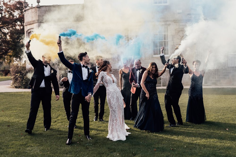 Luxe bride and groom with smoke bomb wedding party in front of stately home elmore court in the cotswolds for a party wedding