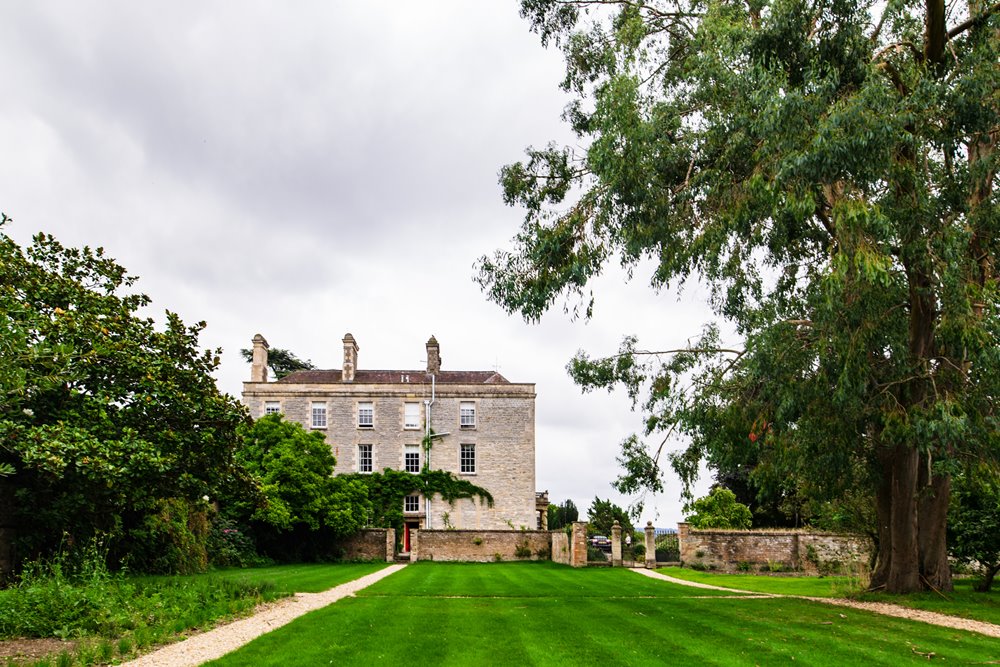 Walled garden with tall trees and mansion house in the background at Cotswolds wedding venue