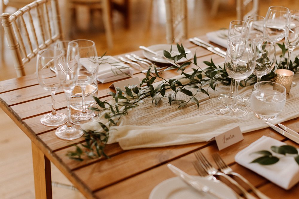 Natural wedding decor of sprigs of greenery and linen on wooden tables at an eco wedding in the cotswolds