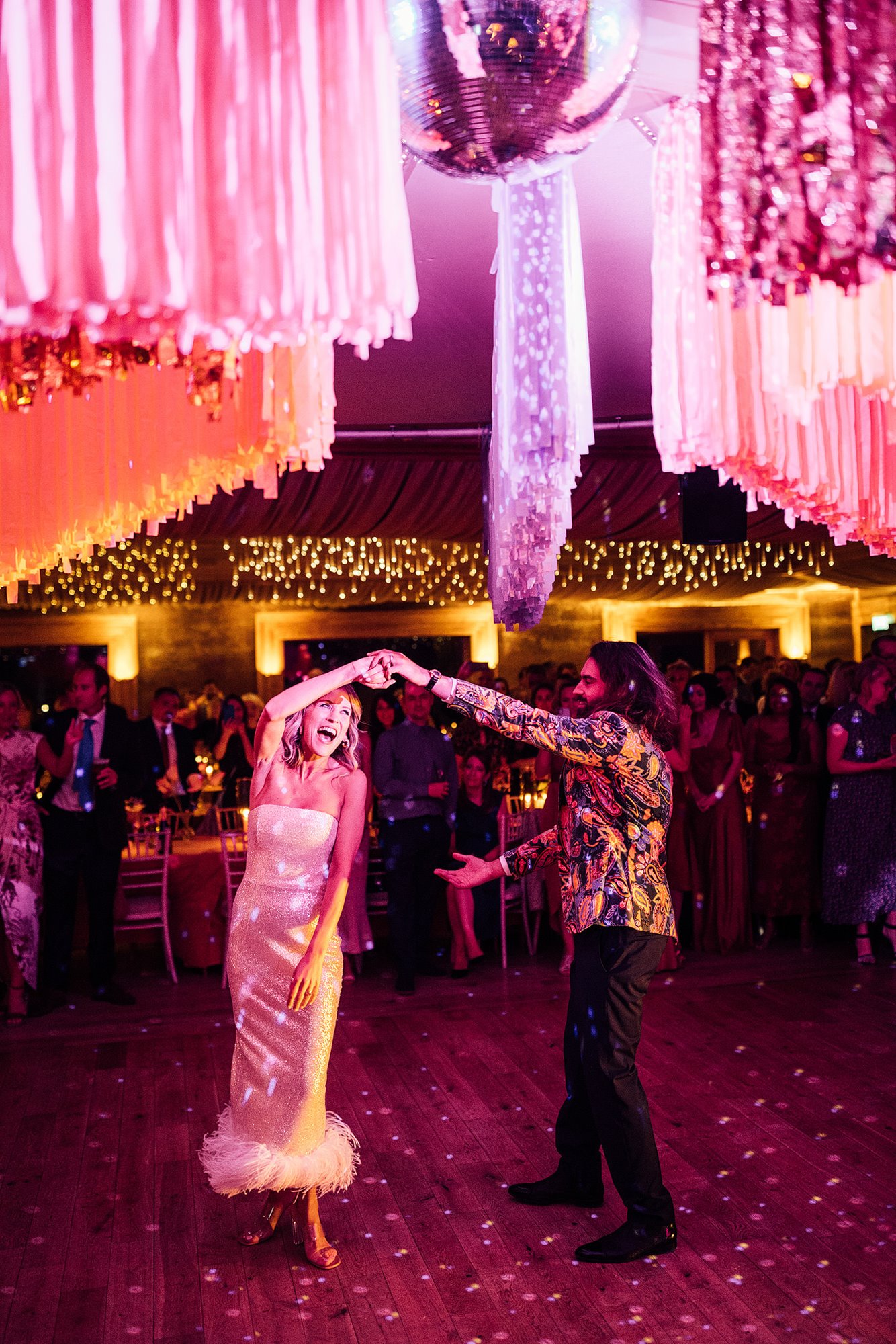 Retro disco wedding first dance with couple dressed in cool party outfits and streamers and disco ball
