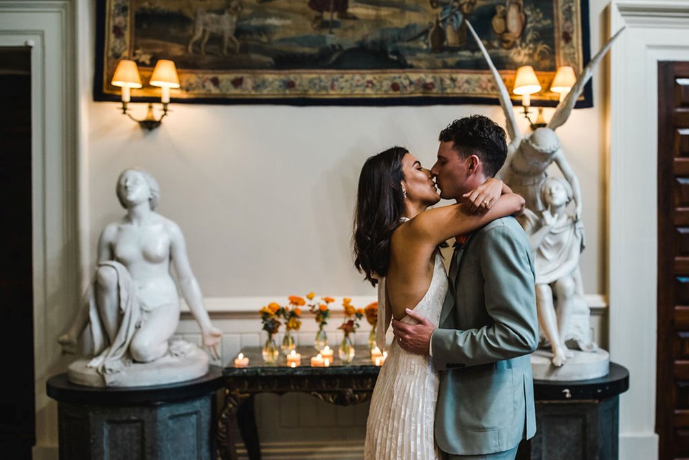 Newlywed couple kiss in front of angel statues in the hall at Elmore court at their micro wedding ceremony in the pandemic