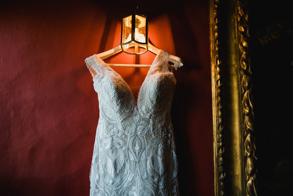 Lace wedding dress hanging on red wall at elmore court