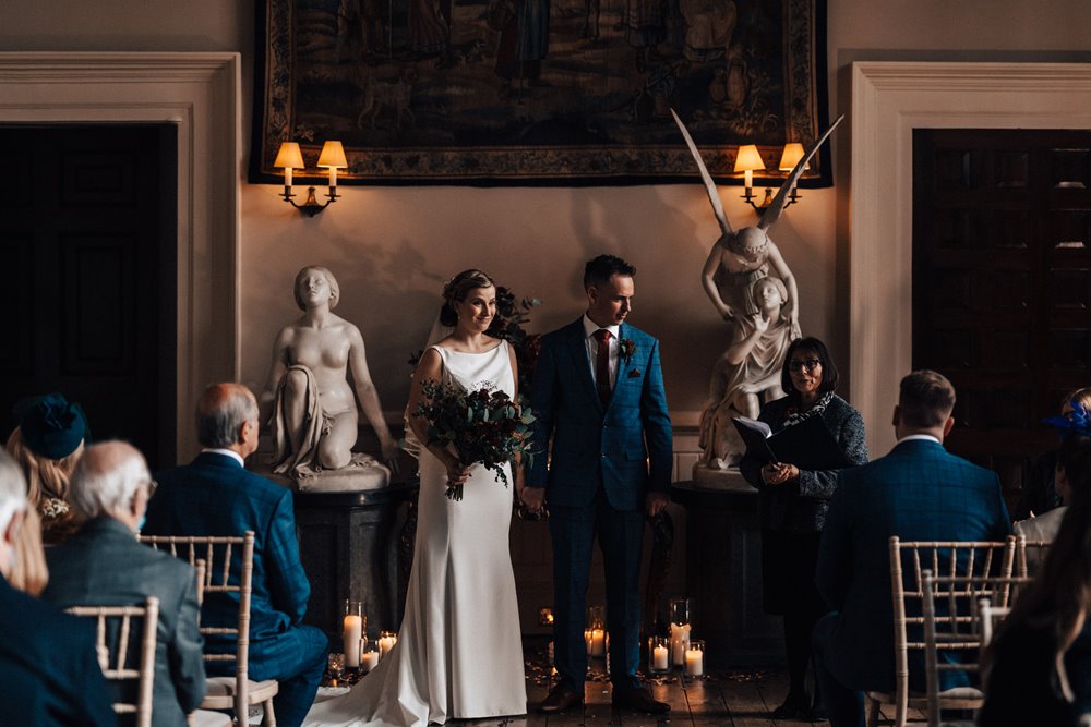 christmas wedding ceremony with candles and angel statues in a stately home hall in the cotswolds