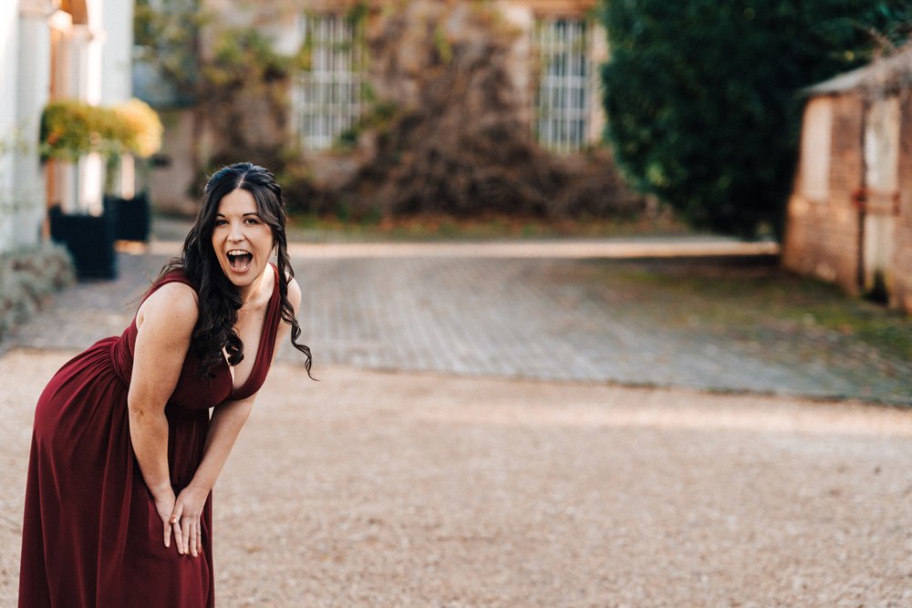 Smiling bridesmaid in burgundy for a christmas wedding outside winter wedding venue elmore court