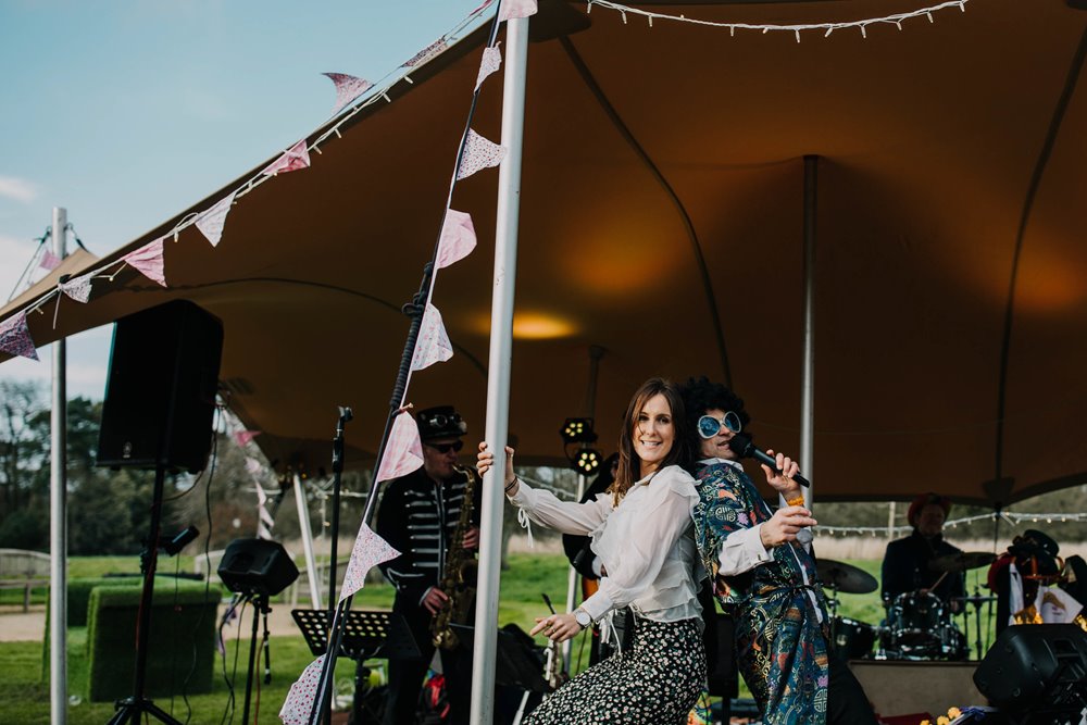 Festival wedding tent with bunting and band performing in dress up clothes and wedding coordinator dancing along at elmore court wild wedding venue in the Cotswolds