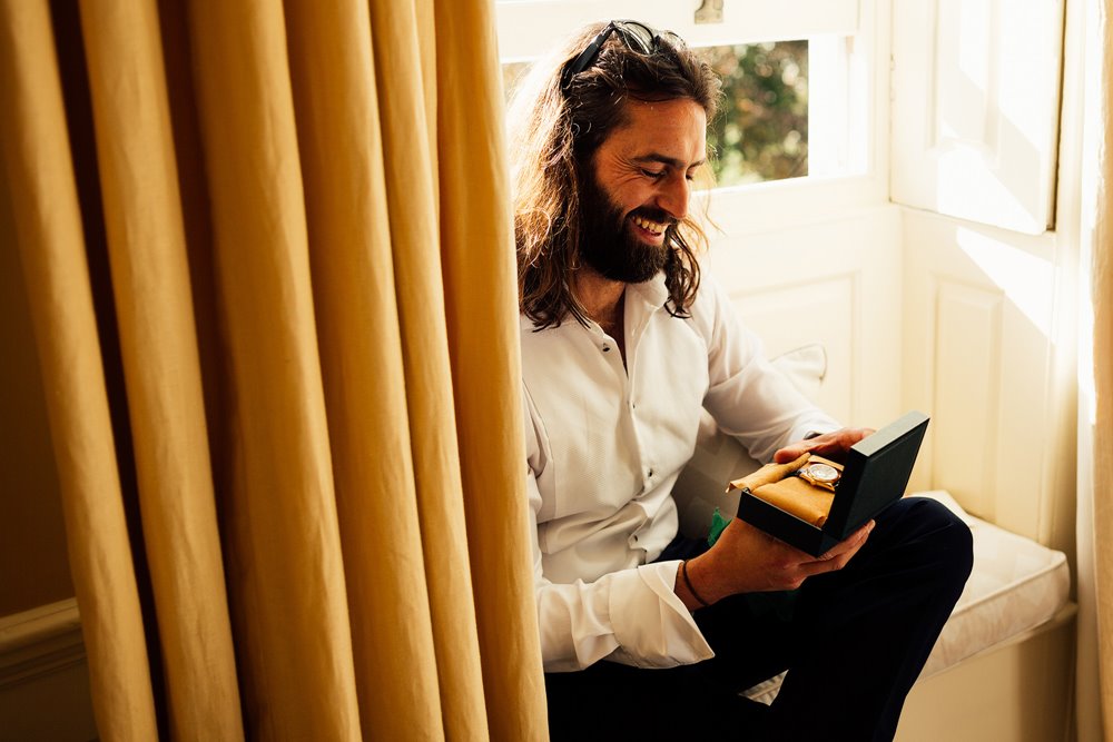 Cool groom with long hair opening a gift from wife to be on wedding morning