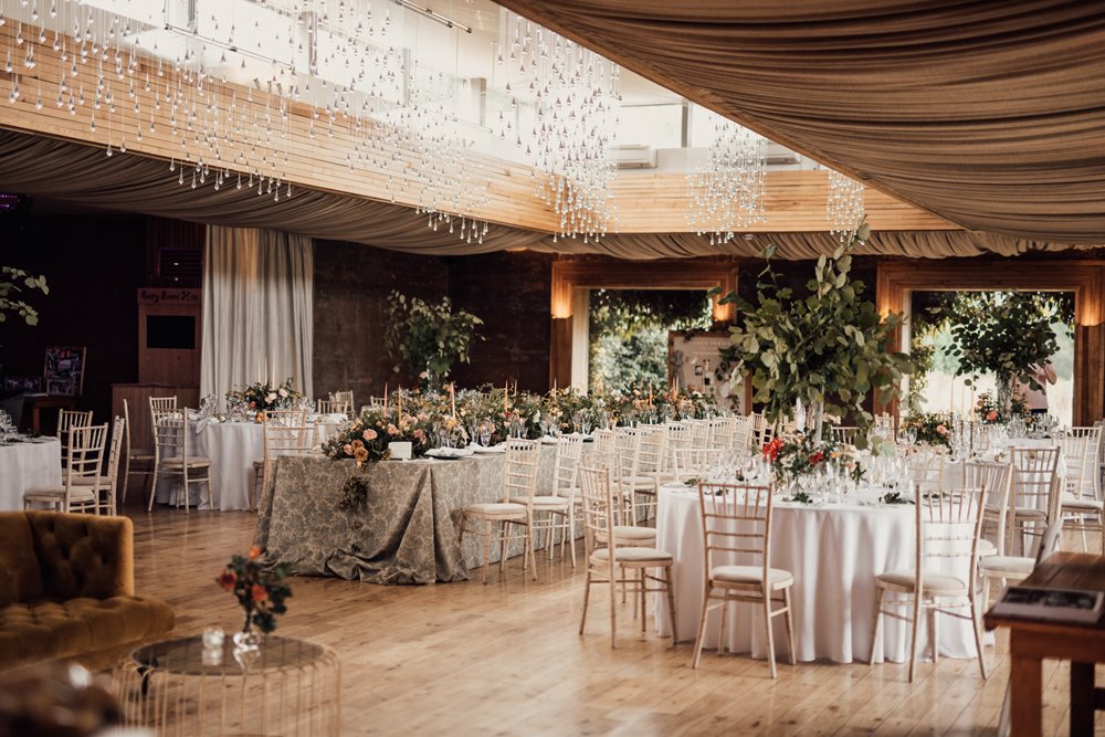 Magical eco wedding reception with ceiling lights and wooden floor with round and long tables decorated with september flowers for a wild wedding fair to celebrate harvest in Gloucester
