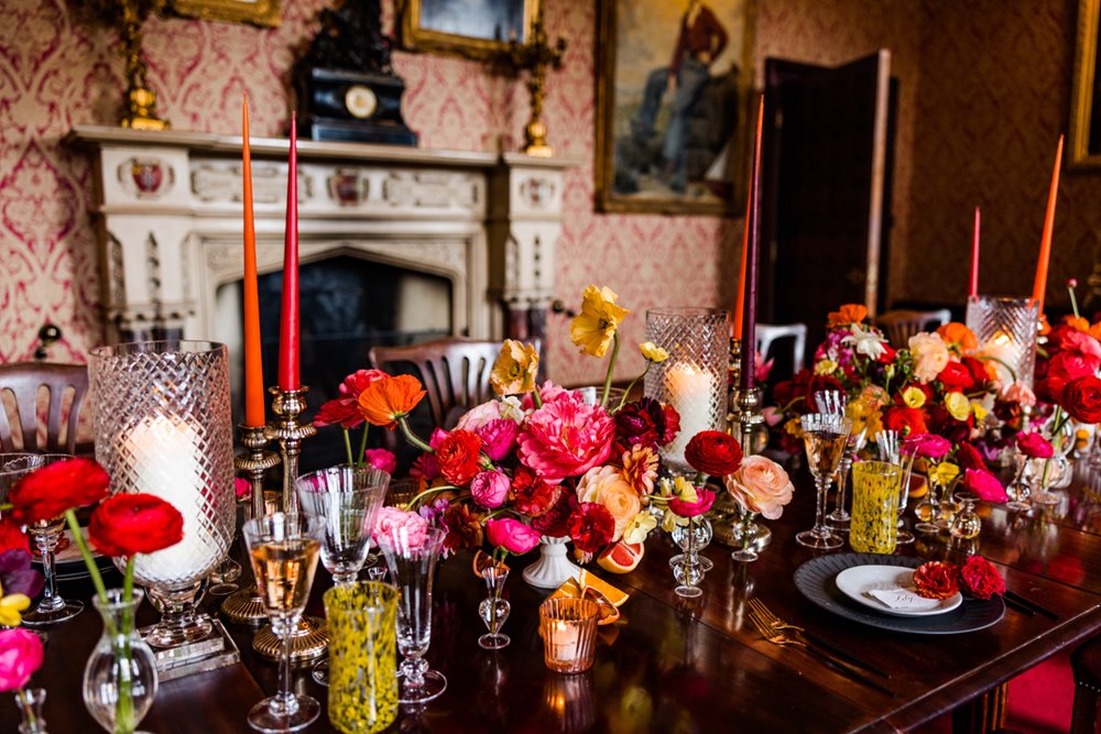 Tall red and pink candles and bold florals adorn the red dining room of unusual stately home wedding venue elmore court for a spring wedding fair in 2022