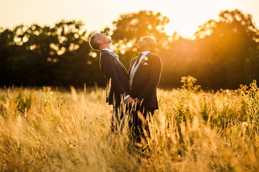 Gay couple hug and laugh at Golden hour in the meadow at eco wedding venue elmore court in the cotswolds