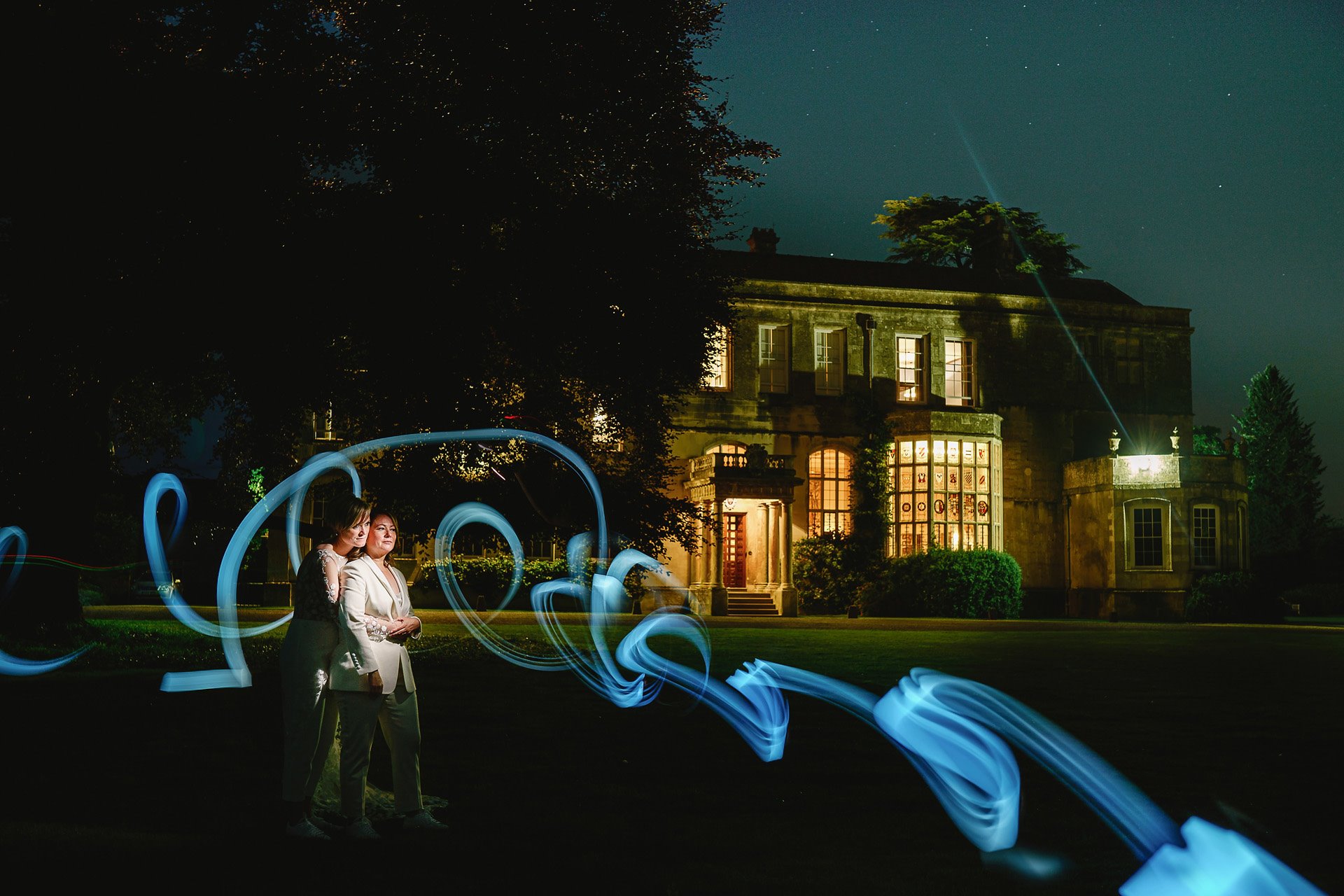 Lesbian wedding couple outside their stately home wedding venue lit up at night