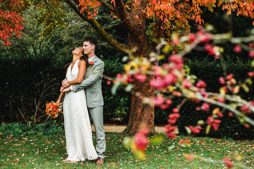 Happy bride and groom laugh under autumn leaves at their micro wedding ceremony at elmore court