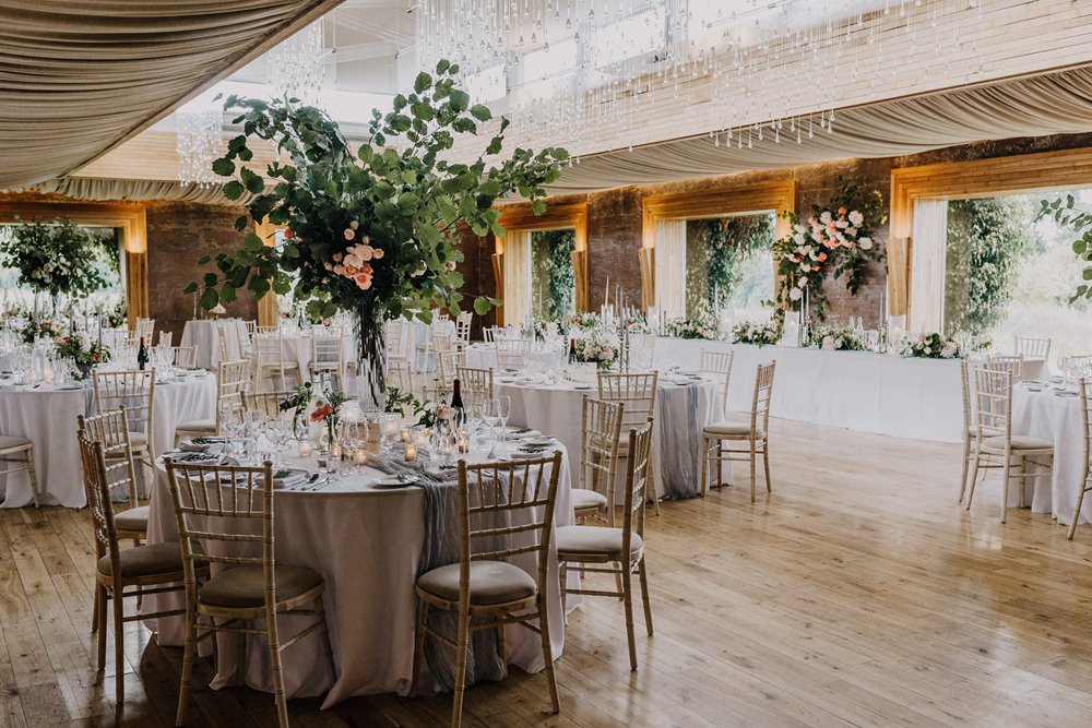 Eco wedding venue The Gillyflower at Elmore Court is a sustainably built soundproof building made of mud and timber from the estate. Greenery decorating round and long tables for a luxe wedding reception 