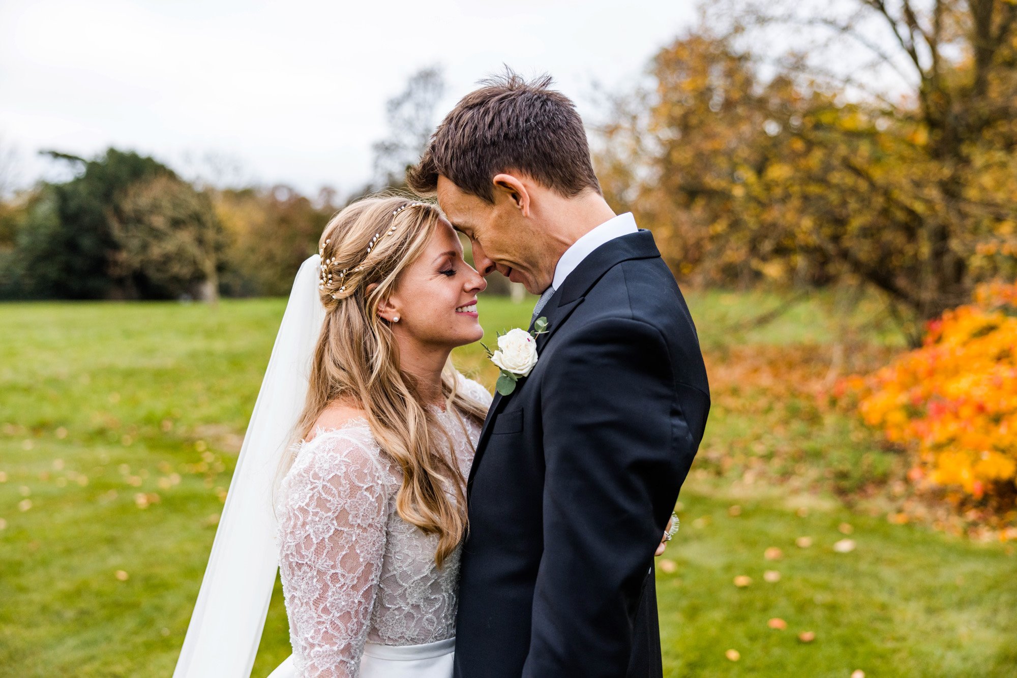 Bride in pearl headpiece and veil touches noses and smiles with her groom outside stately home elmore court on their autumn wedding day