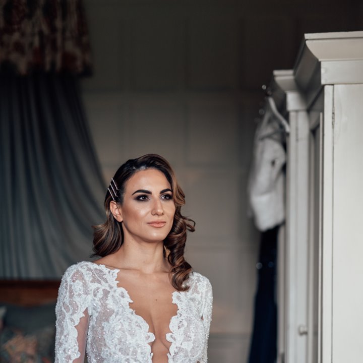 Designer bride standing in stately home bedroom on the morning of her luxe wedding in the Cotswolds