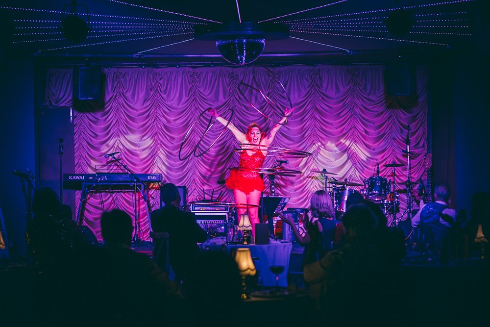 Hoola hoop performer wearing red dress in front of purple curtains at cabaret dinner the parrot cage in the cotswolds