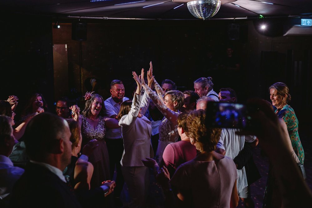 Two brides in the middle of the dance floor surrounded by their wedding guests having the time of their lives at their perfect lgbtq wedding party