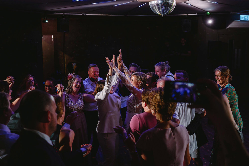 Two brides in the middle of the dance floor surrounded by their wedding guests having the time of their lives at their perfect lgbtq wedding party