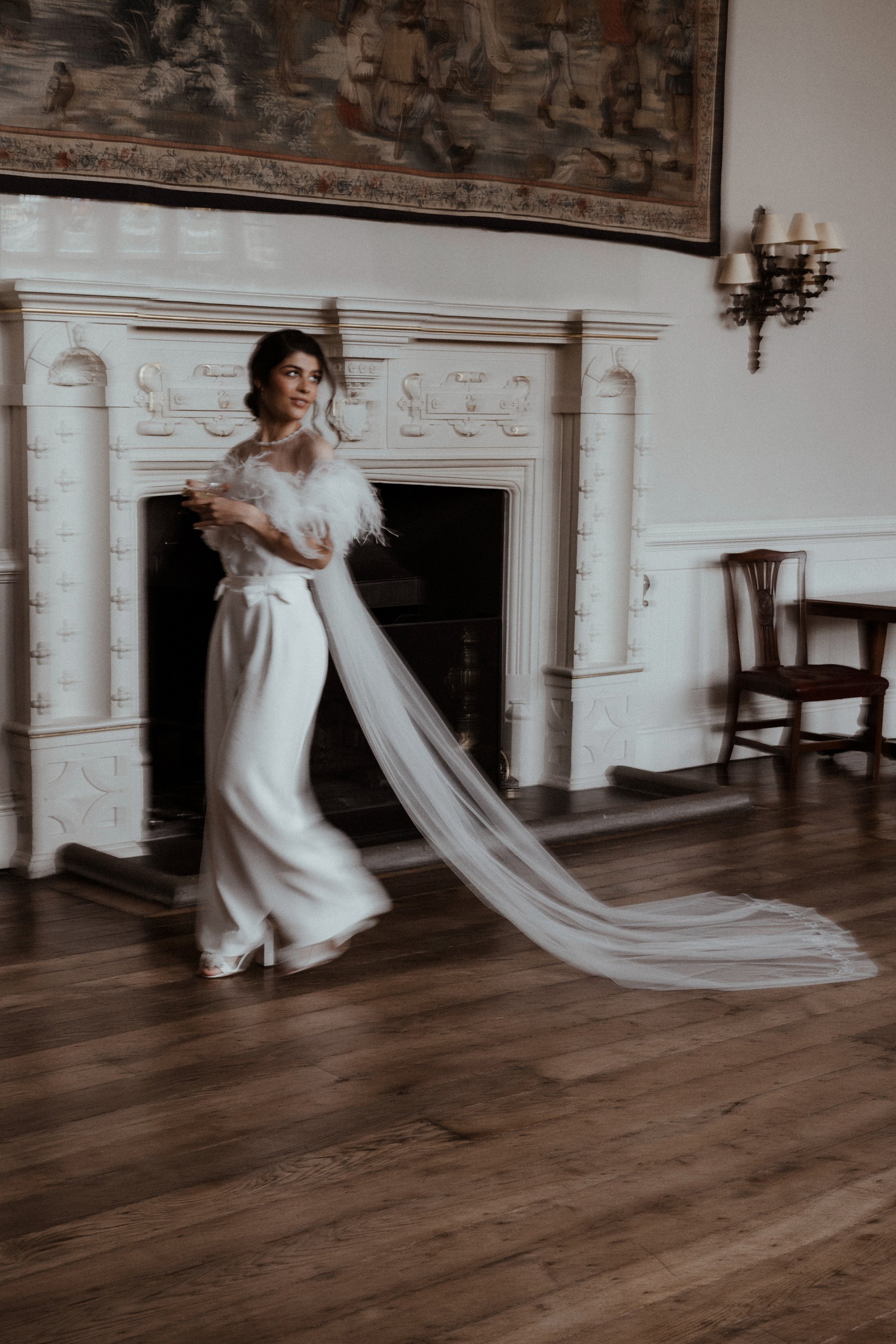 bride in jumpsuit and long veil walking through the great hall at elmore court