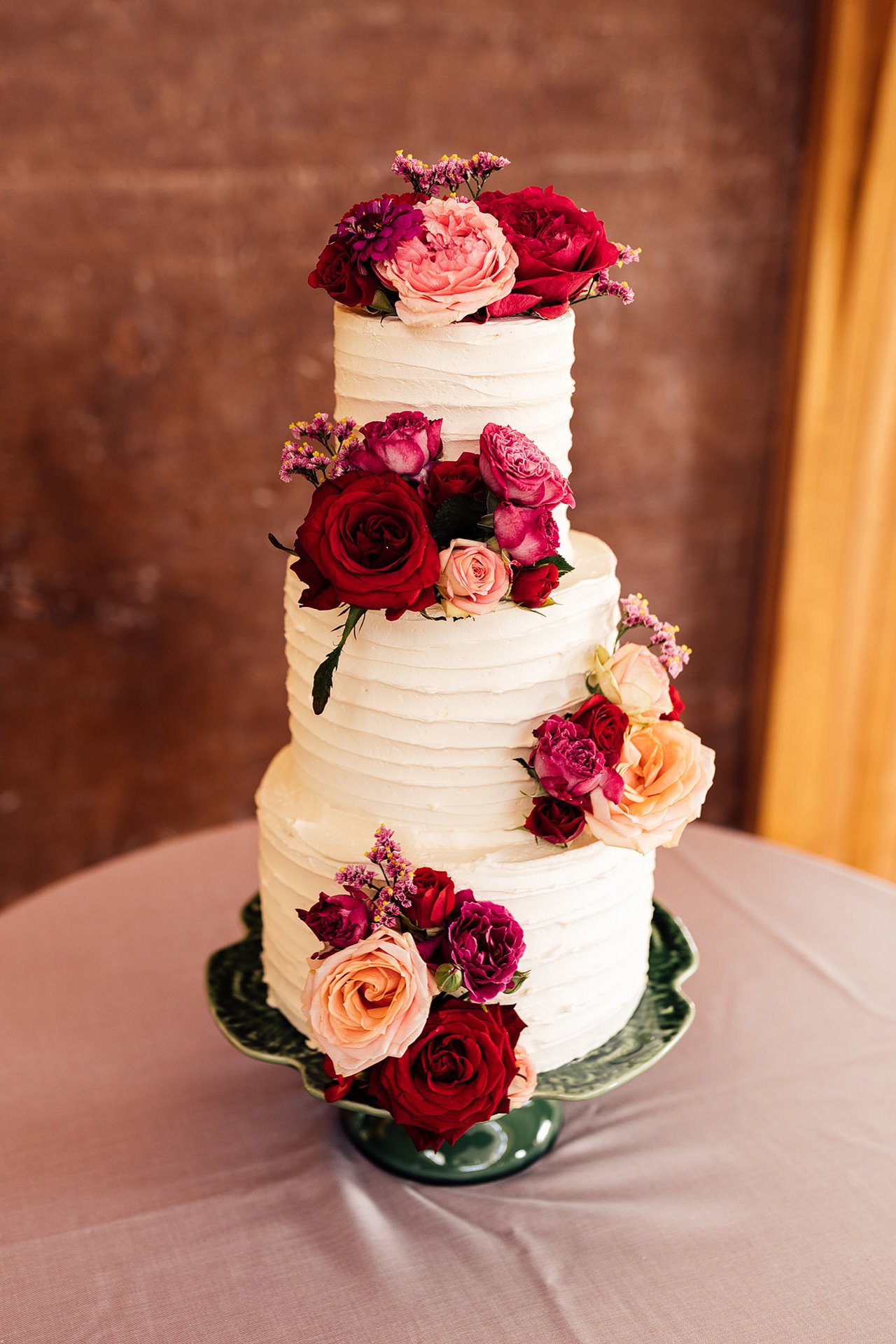 Three tier white wedding cake with real pink and red flowers for fun party wedding reception at cotswolds venue elmore court