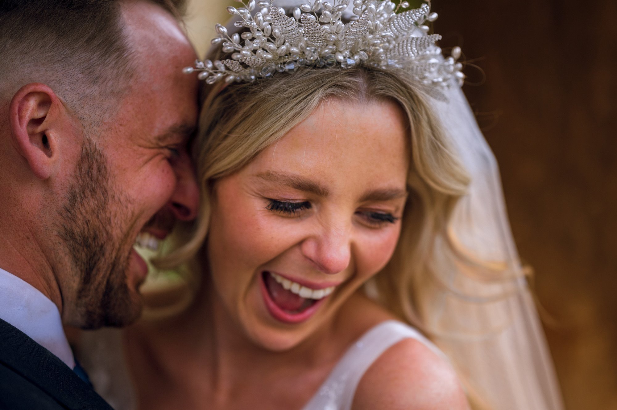 Boho bride in stunning pearl crown and veil laughs as her groom presses face against her face and laughs with her