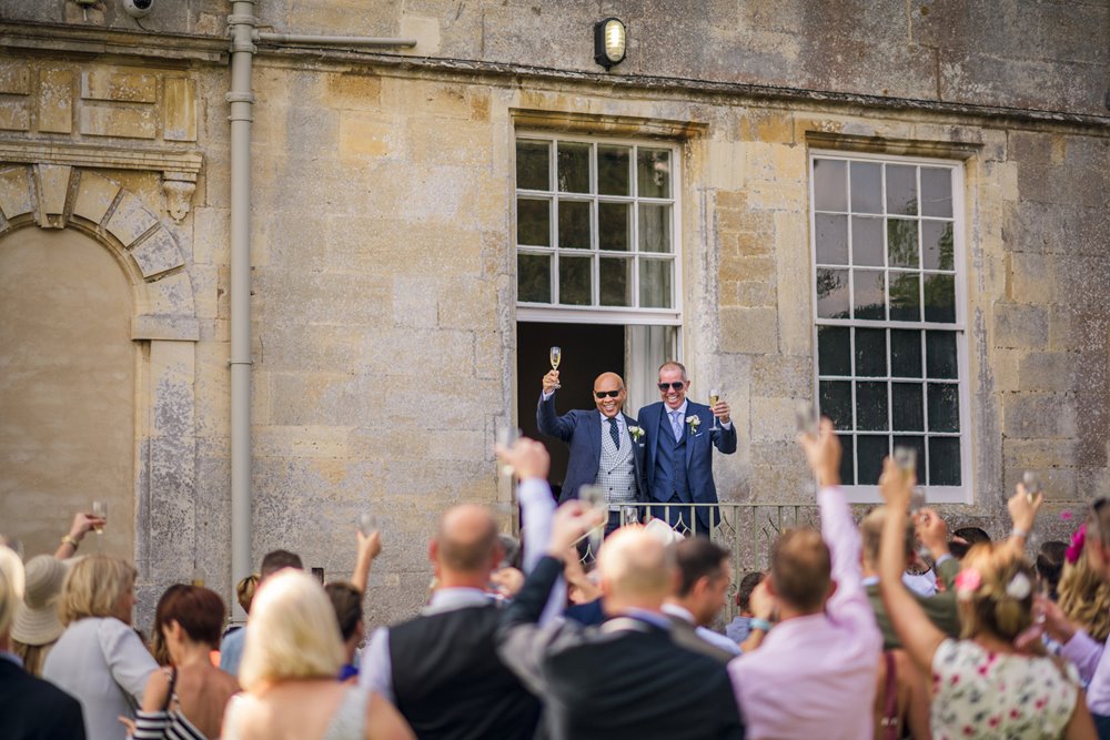 Two grooms in sunglasses get cheered by their wedding guests on the steps as newlyweds