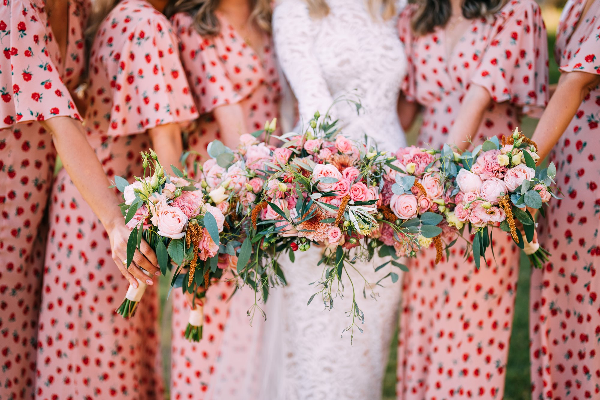 Bridesmaids wearing pink dresses with strawberry pattern holding pink bouquets to the camera at a cool wedding