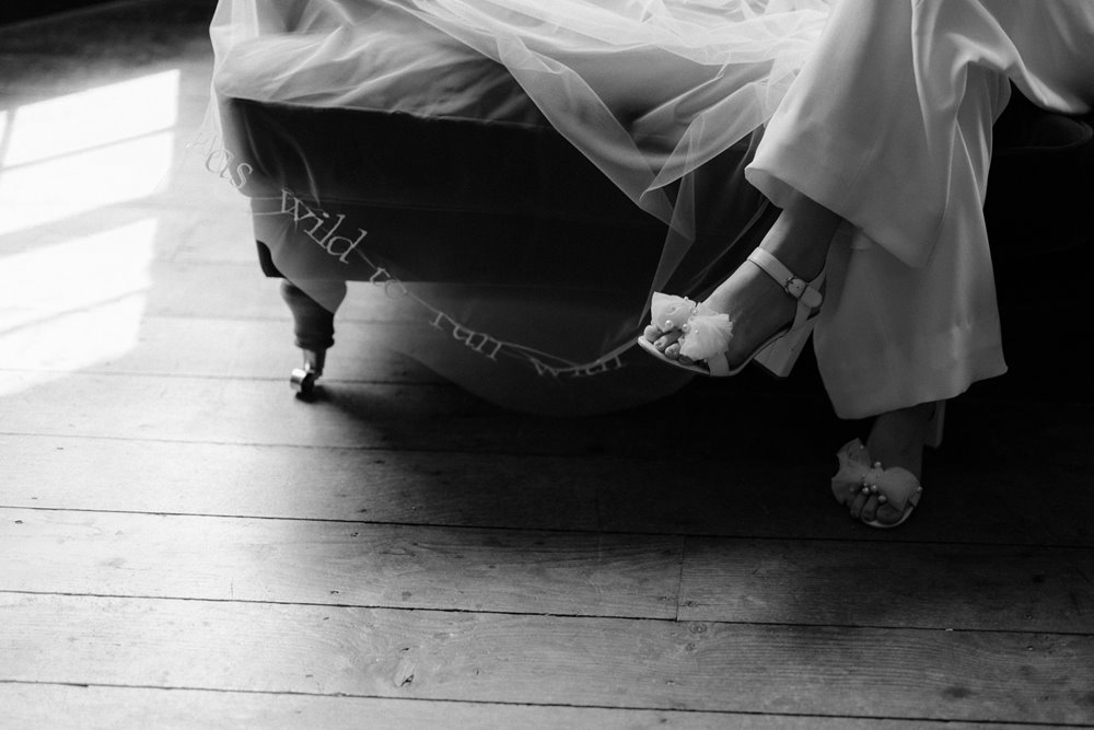 High end wedding inspiration bride sits on chaise lounges in jumpsuit wearing bridal shoes with bows