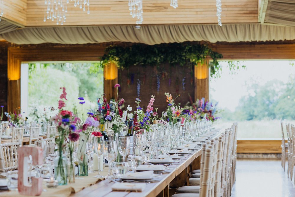 Summer wildflowers adorn long tables for a wedding reception in June