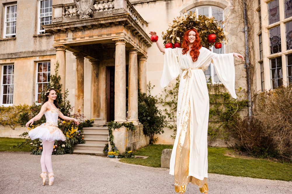 Festival performers on stilts in white outside unusual stately home wedding venue elmore court for a wild wedding fair in 2022