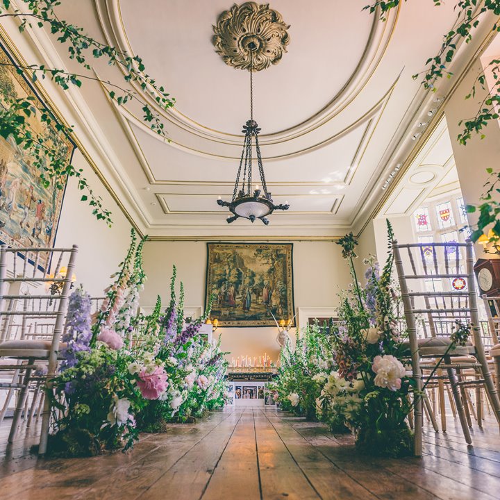 Wild flowers and trees line the aisle of beautiful wedding hall in a stately home mansion house in the cotswolds 