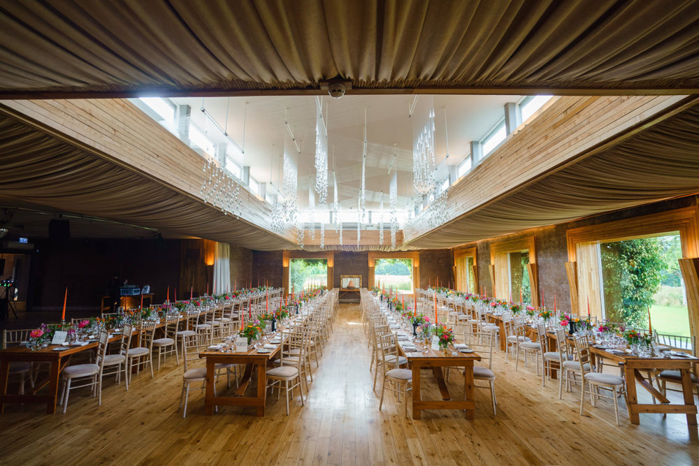 Huge wedding reception for 200 guests with long banqueting tables decorated with pink and orange flowers and candles