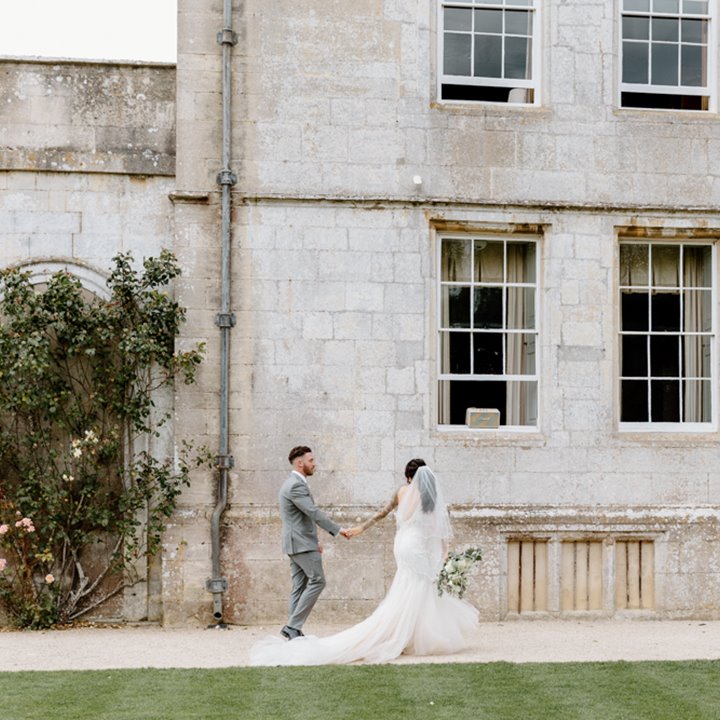 Couple holding hands in front of stately home wedding venue in the cotswolds