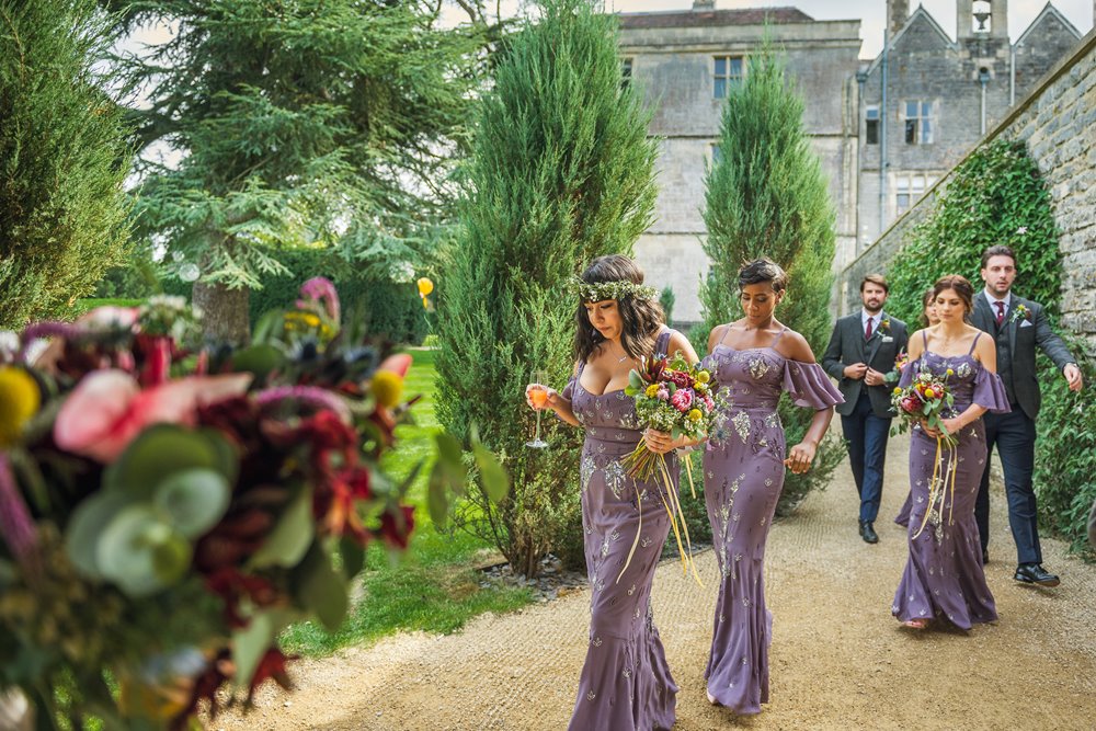 Purple bridesmaids walk into wedding reception holding colourful bouquets