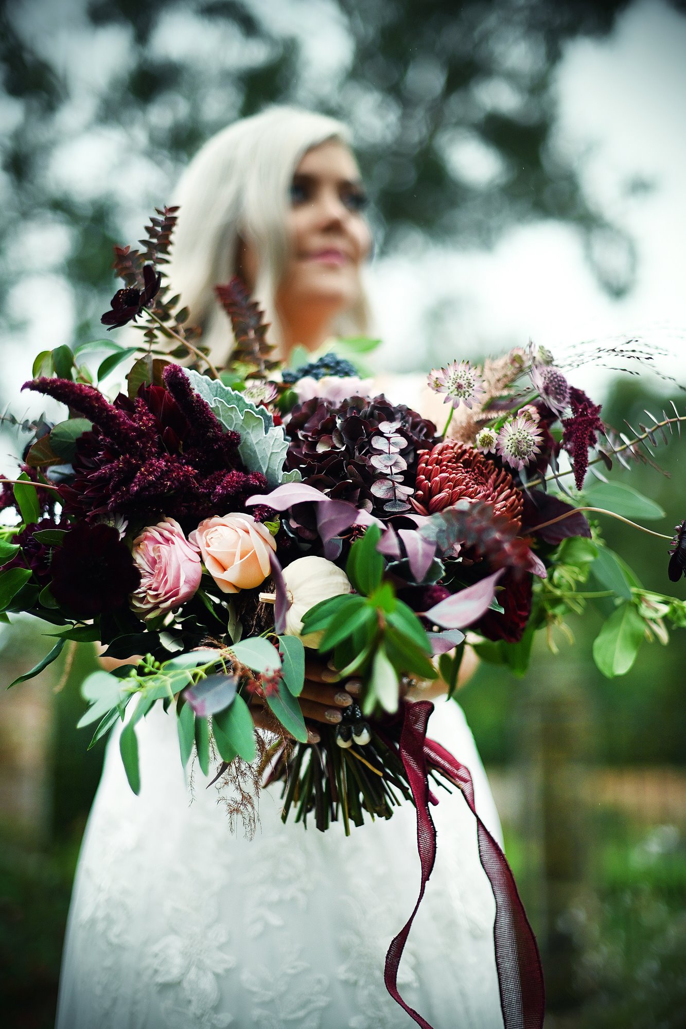 Autumn bride holding deep berry coloured bouquet for her october halloween inspired wedding