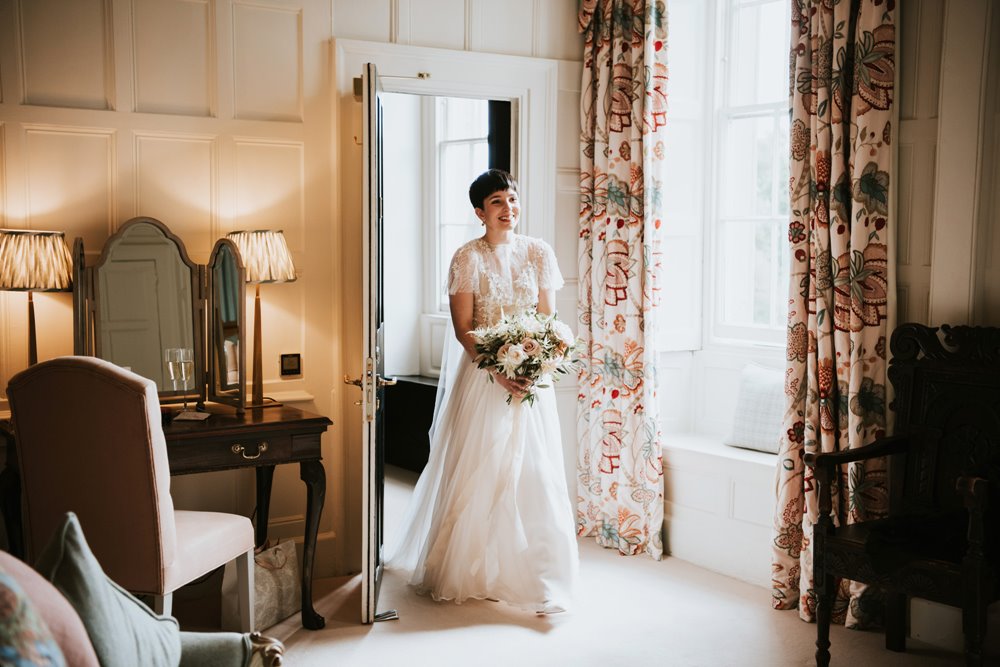 Beautiful bride with short hair wears long white wedding dress in stately home wedding venue bedroom