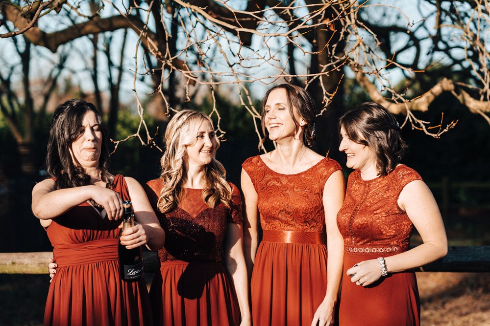 bridesmaids in burgundy popping corks under the beech tree for christmas wedding at elmore court