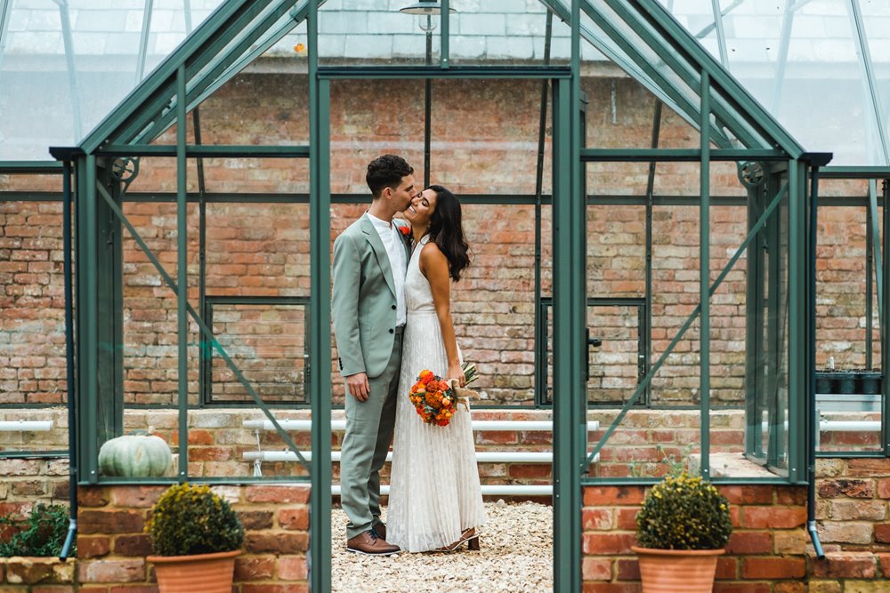Bride and groom kiss in a glasshouse at a micro wedding at elmore court