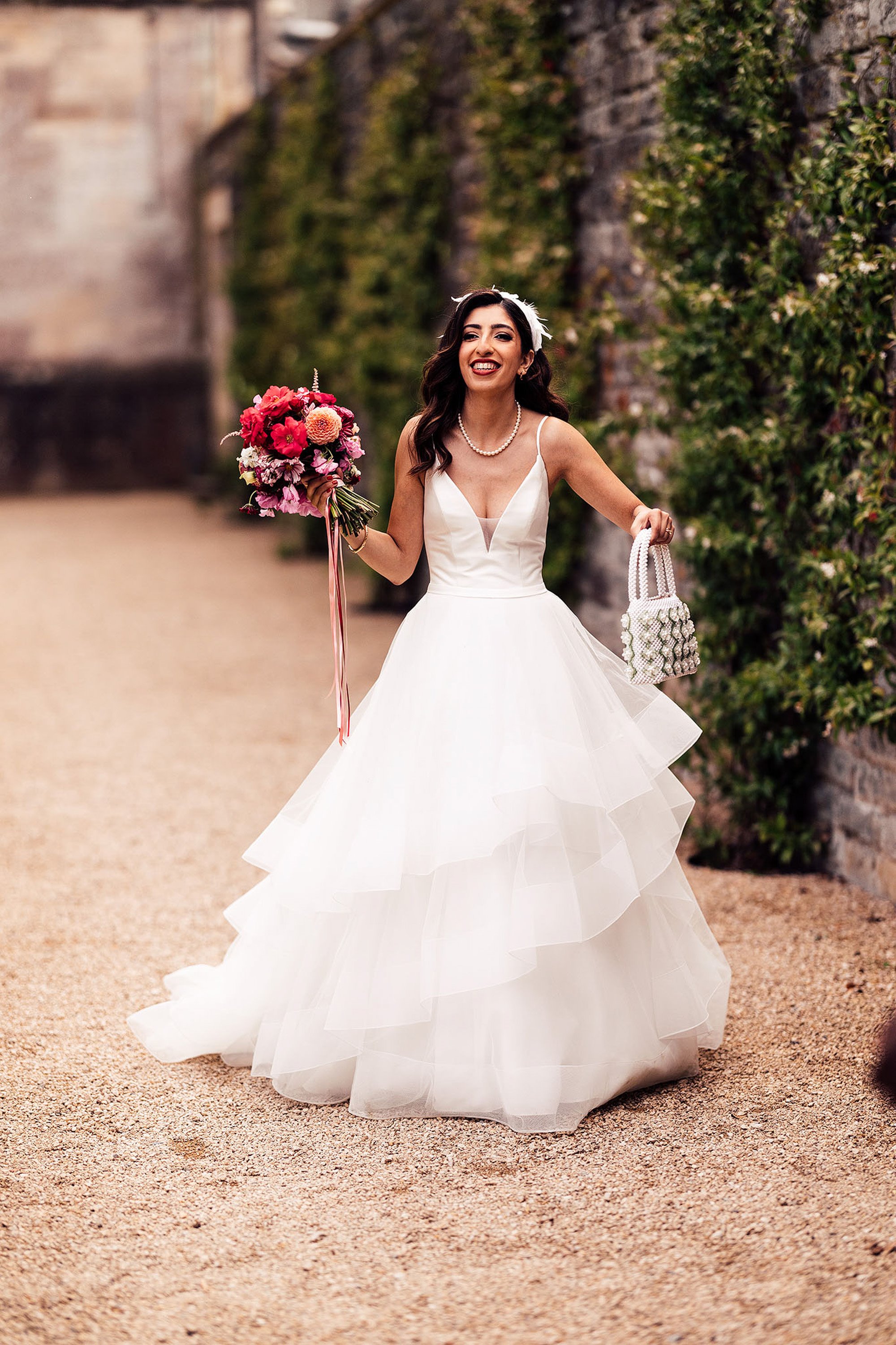 Beautiful modern persian bride in pearl necklace holding pearl bag and bright pink and red bouquet