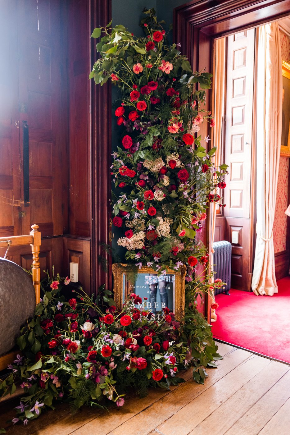 Beautiful bold red flower wall with greenery foliage to match red carpets in mansion house wedding venue elmore court for a wild wedding fair in 2022