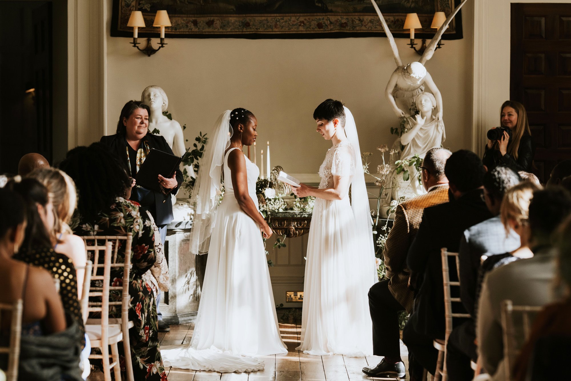 Wedding ceremony in a stately home with two brides standing facing each other reading vows