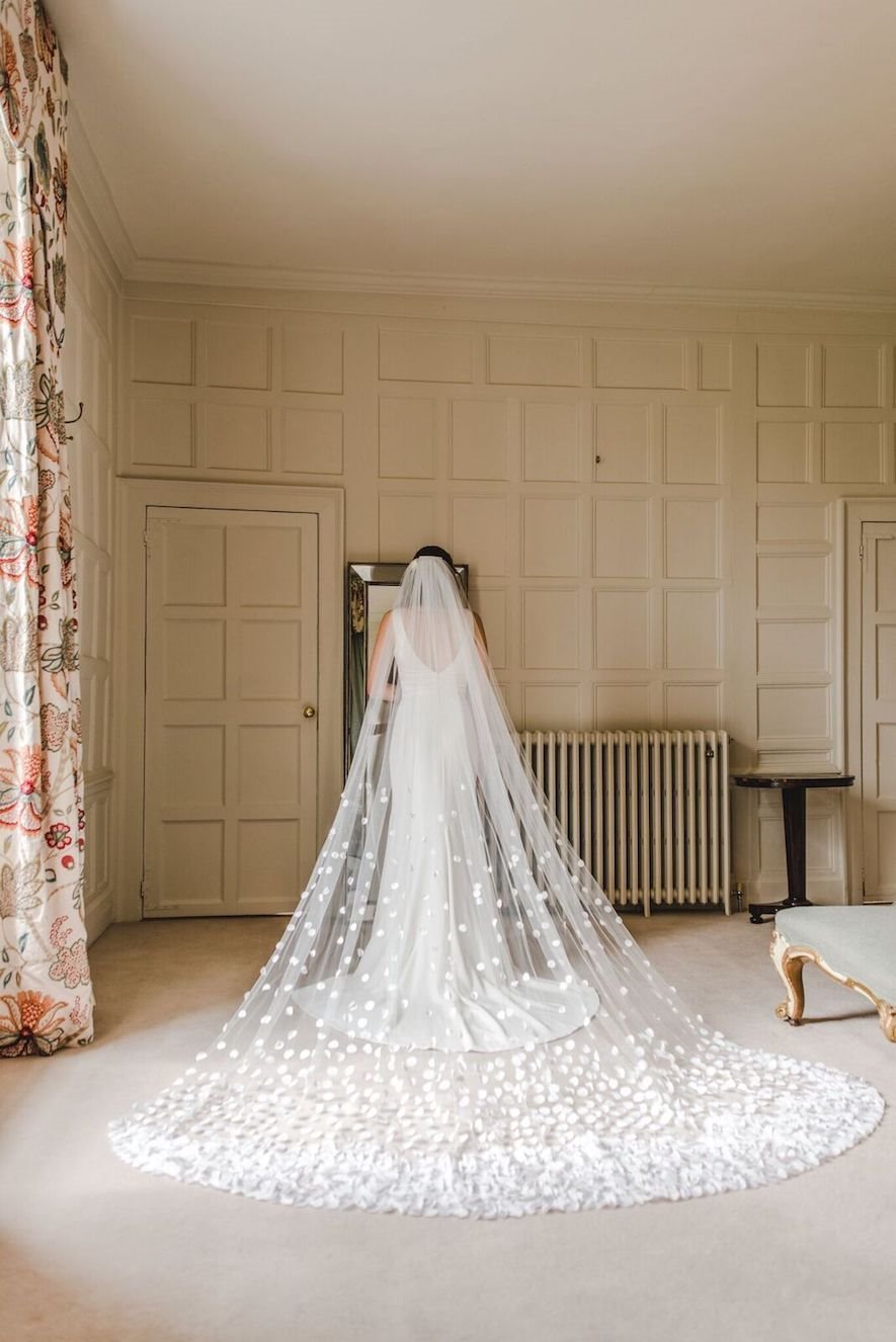Bride in Long wedding veil with petal embroidery standing in stately home wedding venue bedroom