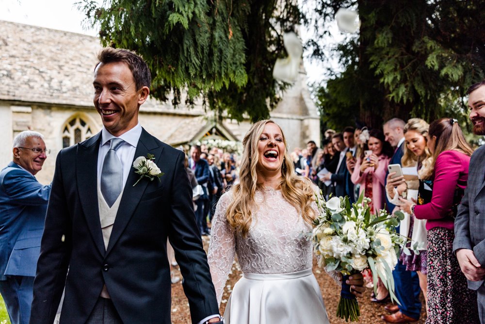 Happy newlyweds laugh and smile leaving church at elmore gloucestershire 