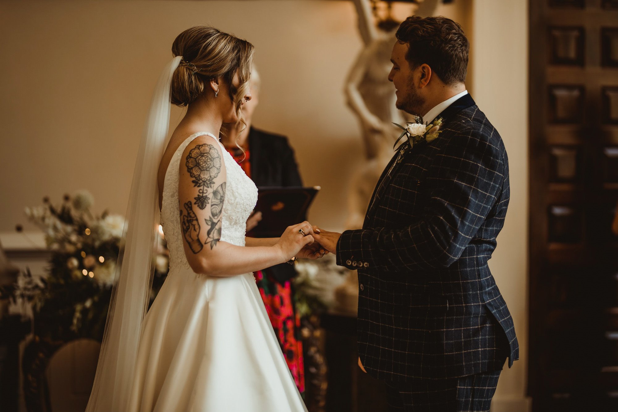 Tattooed bride and groom in tweed suit at their wedding ceremony in stately home 