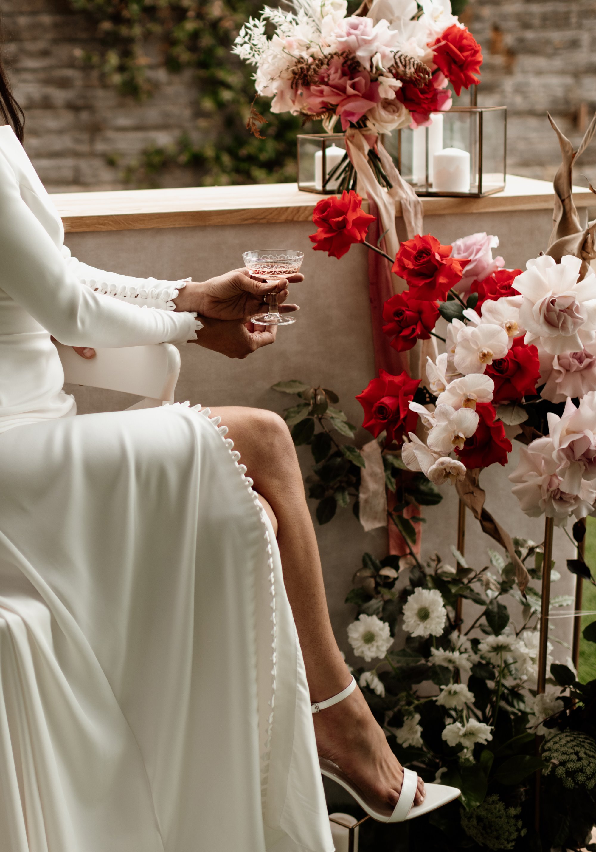 Bride sipping champagne next to a display or red, pink and white wedding flowers