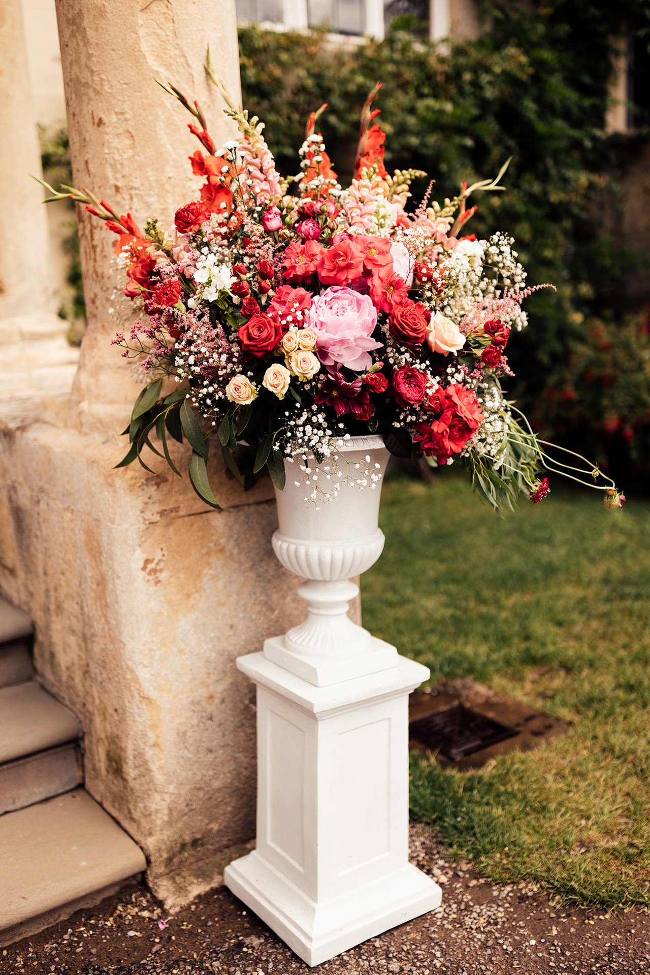 pink and red wedding flowers in a huge urn decorating mansion house steps of elmore court in the cotswolds for a fun Persian wedding